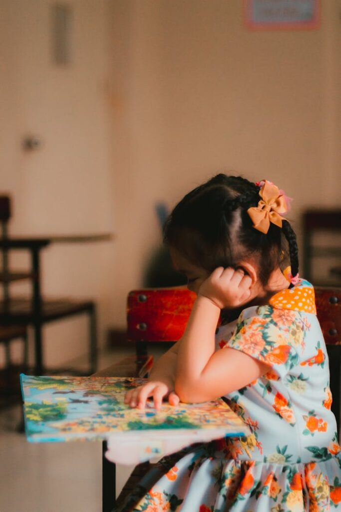 A young girl engrossed in reading a book in an indoor classroom setting.