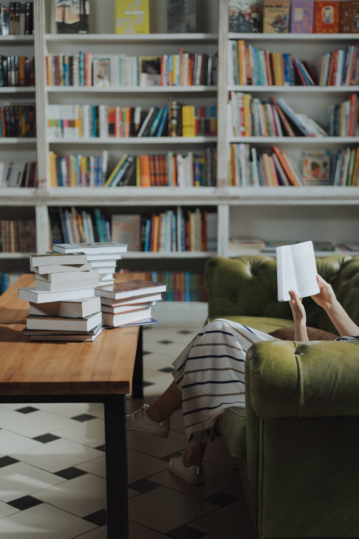 Relaxing with a book in a cozy home library with stacked books.
